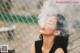 A woman is smoking a cigarette behind a fence.