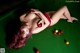 A woman laying on top of a pool table holding a red ball.