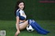 A woman in a blue and white uniform sitting on a soccer ball.