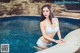 A woman in a white bikini sitting by a swimming pool.