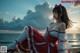 A woman in a red and white dress sitting on the beach.